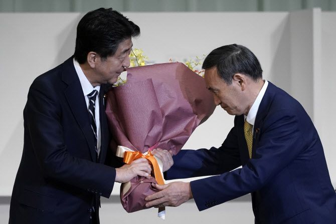 아베 신조 일본 총리(오른쪽)가 자민당 신임 총재로 선출된 스가 요시히데 관방장관에게 꽃다발을 건네고 있다(사진=AFP)