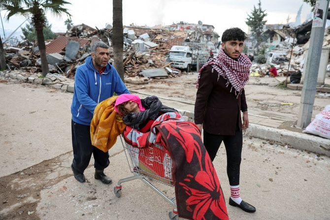 7일(현지시간) 튀르키예 남동부 하타이에서 주민들이 지진으로 부상한 한 여성을 쇼핑카트에 태워 옮기고 있다. (사진=로이터)