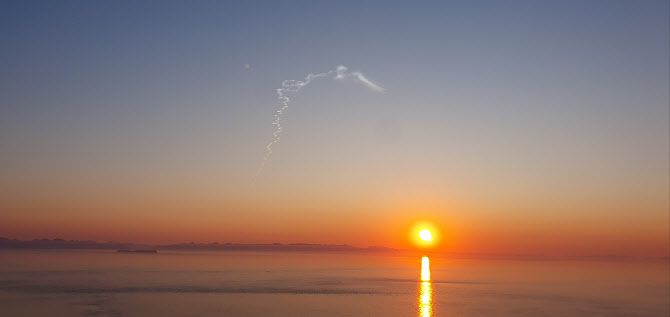 26일 오전 일출 무렵 백령도 끝섬 전망대에서 한 주민이 바라본 동쪽 하늘에 하얀 연기가 길게 뻗어 있다.(사진=연합)