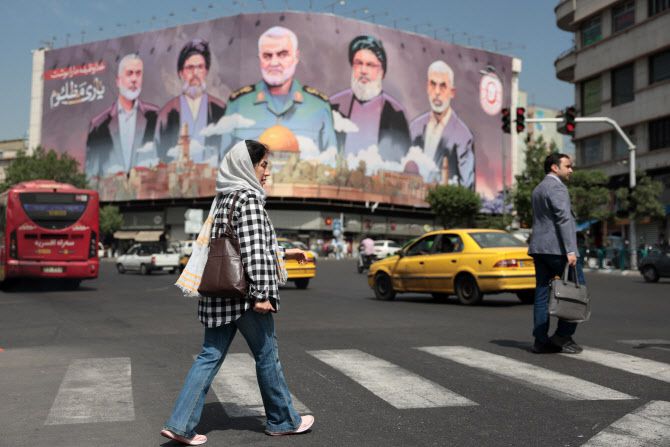 한 여성이 11일(현지시간) 테헤란의 엥겔라브 광장에서 이란과 레바논의 암살된 지도자들의 초상화가 담긴 광고판 앞을 지나가고 있다/