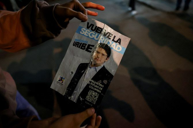 7일(현지시간) 콜롬비아 보고타에서 열린 선거운동 행사에서 야당인 민주센터당의 미겔 우리베 투르바이 콜롬비아 상원의원이 총격을 받은 지역에서 한 사람이 선거 포스터를 들고 있다.(사진=로이터)