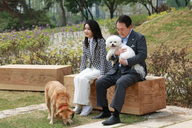 윤석열 대통령과 부인 김건희 여사가 4일 서울 용산 대통령실의 앞마당에 조성된 용산 어린이정원 개방 기념식수를 마친 뒤 써니와 은퇴안내견 새롬이(왼쪽)와 휴식을 취하고 있다(사진=대통령실 제공).