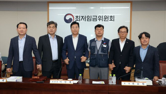 이인재 최저임금위원장(왼쪽 두 번째)이 10일 정부세종청사에서 열린 제12차 전원회의에서 내년 최저임금을 시간당 1만320원으로 17년만에 합의로 결정한 뒤 공익위원-사용자위원-근로자위원과 손을 잡고 있다.(사진=연합뉴스)