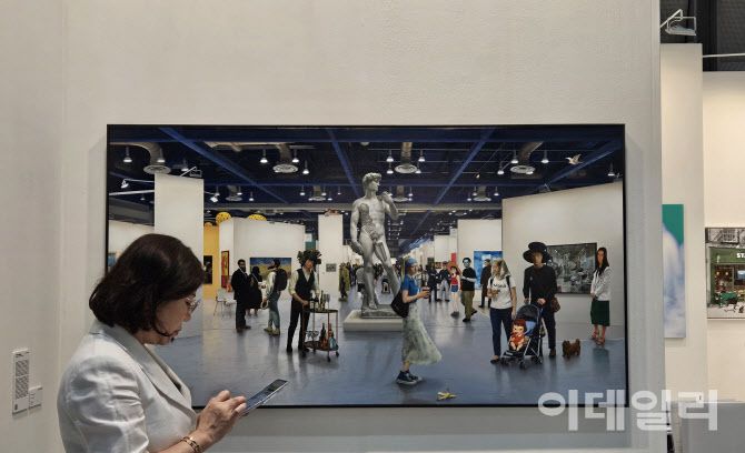 ‘키아프 서울 2025’ 전경. 관람객 옆으로 권능의 ‘투 폴리시드 캄(To Polished Calm, 2025)이 걸렸다. 아뜰리에아키에 걸린 이 작품은 마치 지금 서 있는 아트페어 현장을 옮겨놓은 듯한 정밀한 묘사로 관람객들의 눈길을 끌었다(사진=오현주 문화전문기자).