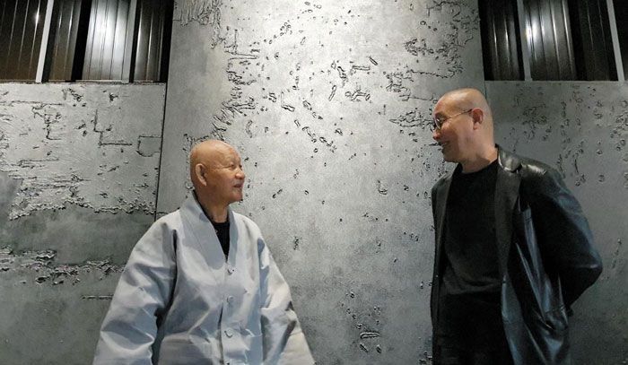 통도사 방장 성파 스님(왼쪽)과 김아타 작가. 김 작가는 성파 스님으로부터 받은‘아타’라는 법명을 작가명으로 쓰고 있으며, 22년 전 스님과 만남에서 삭발한 후 지금까지 머리를 깎은 채 지낸다. 두 사람 뒤로 보이는 것은 포사격을 받아 찢어진 캔버스를 수거해 만든 김씨의 작품. /김한수 기자