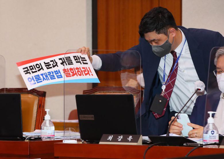 25일 서울 여의도 국회에서 열린 법제사법위원회 전체회의에서 법사위 관계자가 국민의힘 의원들이 퇴장한 뒤 남겨져 있던 '언론중재법' 반대 손팻말을 정리하고 있다. /연합뉴스