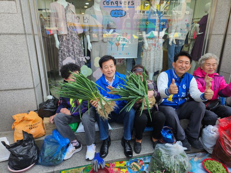정동영 전 통일부장관이 9일 영동군 시장을 방문해 이 지역의 더불어민주당 이재한 후보를 응원했다. 사진은 정 전 장관(왼쪽에서 두 번째)이 대파를 들고 이 후보(왼쪽에서 네 번째)와 상인들 옆에서 포즈를 취하는 모습. /권순완