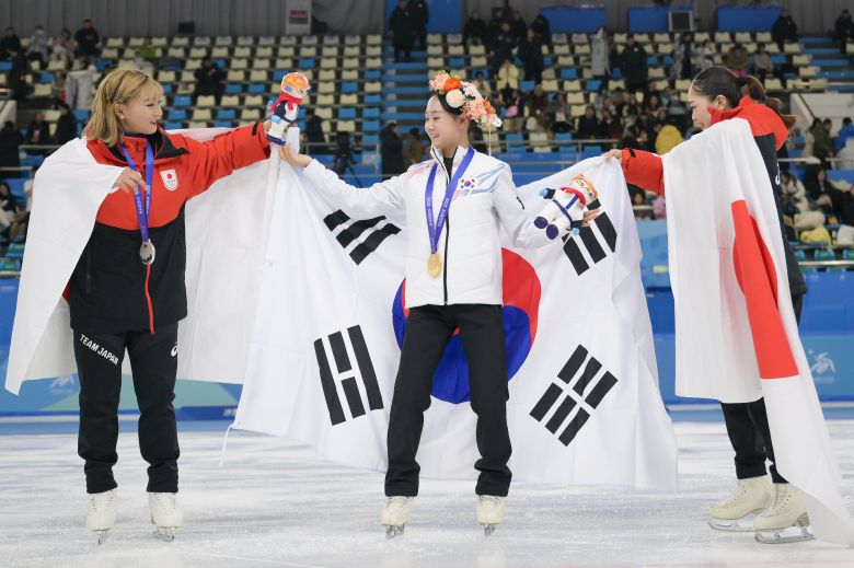 13일 2025 하얼빈 동계아시안게임 피겨 여자 싱글에서 금메달을 획득한 김채연이 은·동메달을 딴 일본 사카모토 가오리와 요시다 하나의 도움을 받아 태극기를 두르고 있다. /신화통신 연합뉴스