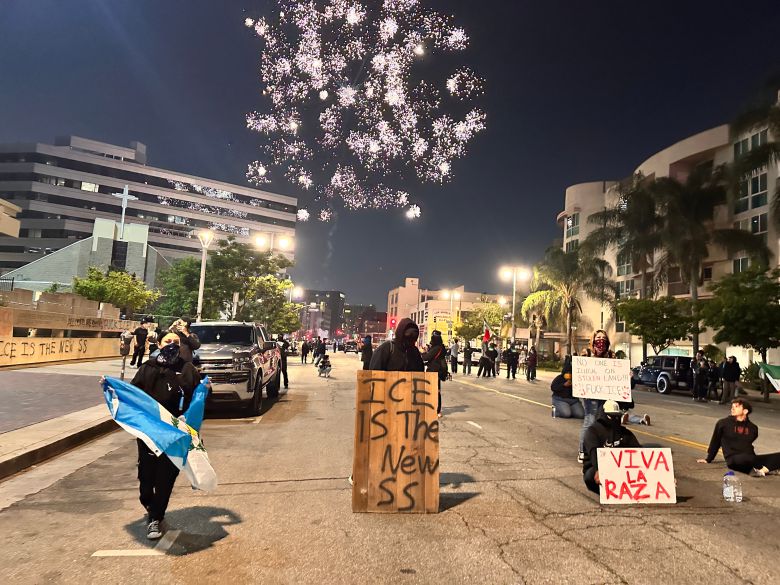 9일 밤 미국 캘리포니아주 로스앤젤레스에서 트럼프 행정부의 이민자 추방 정책에 항의하는 시위대가 미 이민 단속국은 '새로운 나치 친위대(SS)'에 빗대는 팻말 등을 들고 경찰과 대치하고 있다. 밤하늘에서 시위대가 쏘아올린 폭죽이 터지고 있다./오로라 특파원
