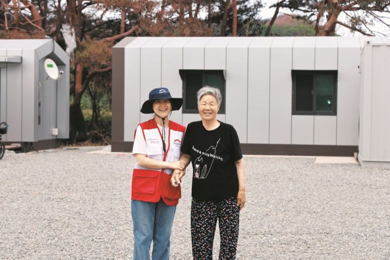 희망브리지 - 경상북도 청송군 희망하우스 앞에서 김분순 어르신(오른쪽)이 희망브리지 직원과 함께 환하게 웃고 있다. /희망브리지 제공