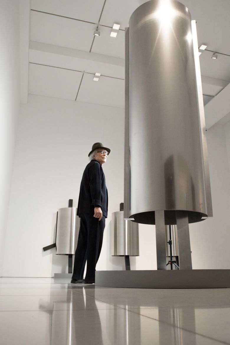 엄태정 조각가가 은빛 원통형 조각 ‘낯선 자의 은신처’ 사이에 서 있다. 알루미늄으로 만든 신작 연작이다. /고운호 기자