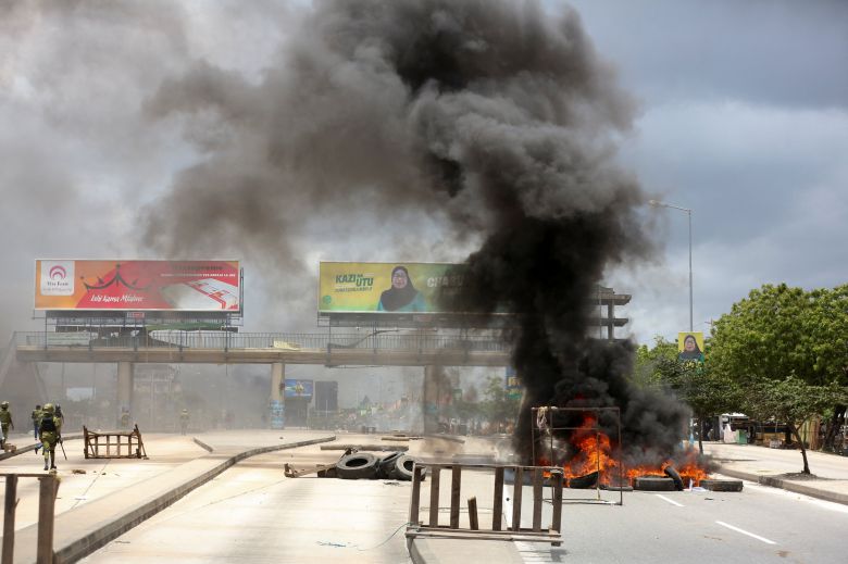30일 탄자니아 다르에스살람의 한 도로를 타이어 더미로 가로막고 불태워 발생한 까만 연기가 하늘로 치솟고 있다. 대선 과정에 분노한 시위대가 방화 등 폭력 시위를 벌이는 가운데 연임이 확실시된 사미아 술루후 하산 대통령의 선거 광고가 연기 뒤쪽으로 보인다. /로이터 연합뉴스