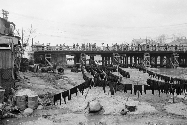 1950년대 서울 청계천 주변은 전쟁을 피해 고향을 떠난 피란민들이 모여 살았다. 판자로 만든 가건물에서 전쟁이 아니라 평화를 바라며 이름 붙인 소규모 봉제 공장들이 오늘날 평화시장이 되었다. 천변에 염색한 옷들이 널려 있다./©한영수_서울 청계천 1958