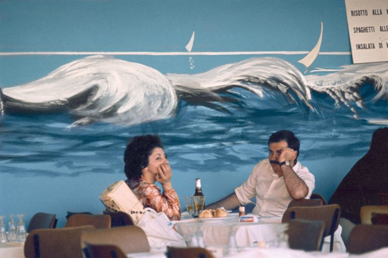 볼로냐의 한 식당 벽에 그려진 파도 그림. 아래 테이블에 무료한 표정의 손님들과 묘한 대조를 이룬다. Bologna, f11, 1125, Natural Light series, 1973, C-print, 23.8×34.8cm, © Heirs of Luigi Ghirri