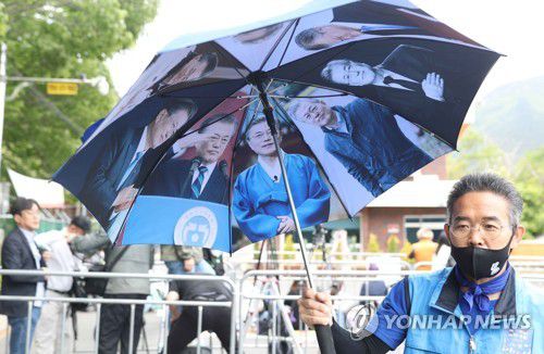 문재인 전 대통령 우산(양산=연합뉴스) 김동민 기자 = 문재인 전 대통령 내외 귀향일인 10일 오전 문 전 대통령 사저가 있는 경남 양산시 하북면 평산마을 평산마을회관 주변에서 한 지지자가 문 전 대통령 사진으로 만든 우산을 소개하고 있다. 2022.5.10 image@yna.co.kr