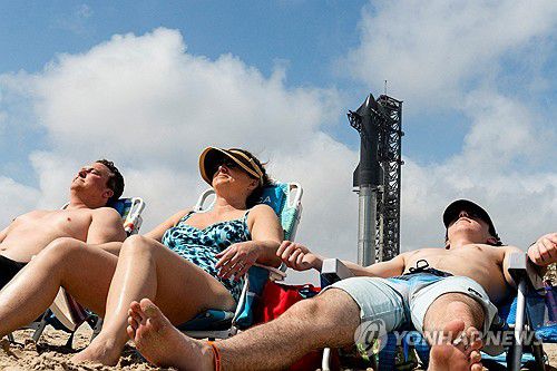 스페이스X의 스타십 발사대를 배경으로 해변에서 휴식을 취하는 사람들[로이터=연합뉴스. 재판매 및 DB 금지]