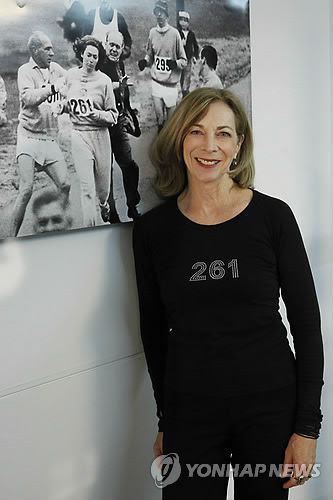 캐서린 버지니아 스위처(서울=연합뉴스) 배경에 걸린 사진은 1967년 보스턴 마라톤에서 달리는 스위처(261번 러너)와 그가 뛰는 것을 중단시키려고 하는 조직위원장(검은 양복)의 모습. [EPA=연합뉴스 자료사진]
