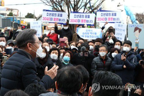 더불어민주당 이재명 대선후보가 2021년 12월 4일 전북 군산시 공설시장을 방문, 시민들에게 지지를 호소할 때 지지자들이 "소년공의 꿈을 3040이 응원합니다"라는 손피켓을 들고 있다. [연합뉴스 자료사진]