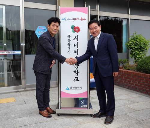 울산시 시니어초등학교 앞에서 박선구 시니어초등학교장(오른쪽)과 악수하며 포즈를 취한 서재우씨.[촬영 허광무]