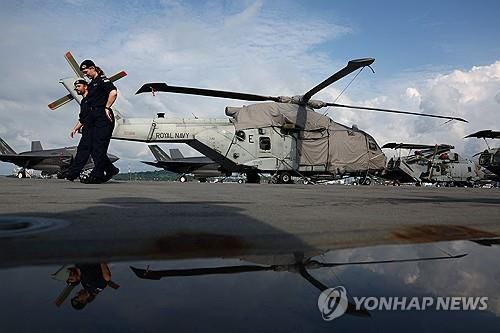 영국 항공모함 함상의 헬리콥터와 군인들(싱가포르 로이터=연합뉴스) 2025년 6월 24일 싱가포르의 마리나베이 크루즈 센터에 입항해 있는 영국 해군 항공모함 '프린스오브웨일스' 함상에 있는 멀린 헬리콥터 옆을 군인들이 지나가고 있다. (REUTERS/Edgar Su) 2025.6.25.
