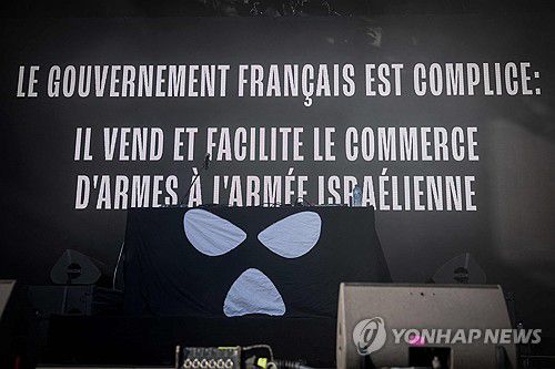 24일(현지시간) 북아일랜드 힙합그룹 니캡이 프랑스 파리 교외 생클루에서 열린 음악 축제에서무대 스크린에 '프랑스 정부는 공범이다' 문구를 띄운 모습.[AFP=연합뉴스]