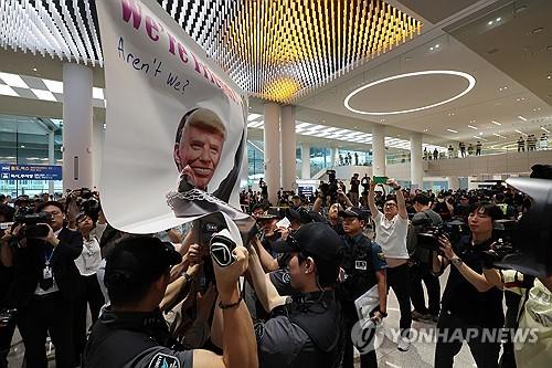 시위 저지하는 공항경찰대(영종도=연합뉴스) 이진욱 기자 = 미국 이민당국에 의해 조지아주에 구금됐던 한국인 근로자들이 귀국한 12일 인천국제공항 제2여객터미널 입국장에서 공항경찰대가 도널드 트럼프 미국대통령 얼굴 배너를 든 시민단체의 시위를 저지하고 있다. 2025.9.12 cityboy@yna.co.kr