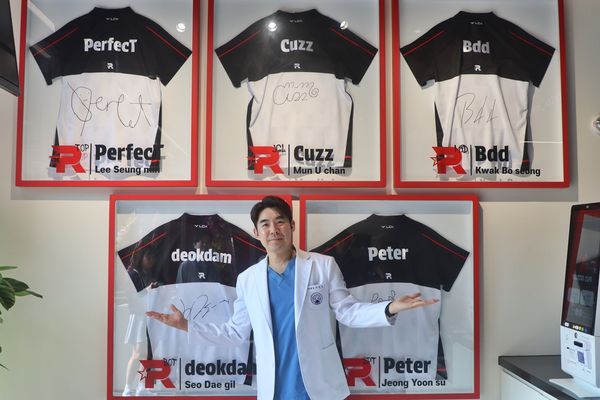 자생한방병원 이진호 병원장이 KT롤스터 카페 벽에 전시된 선수단 친필 사인 유니폼 앞에서 기념사진을 촬영하고 있다.