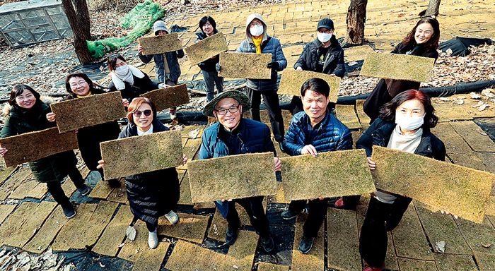 회원들이 천수텃밭 이끼 재배장에서 이끼가 자라고 있는 야자 매트를 들어 보여주고 있다.