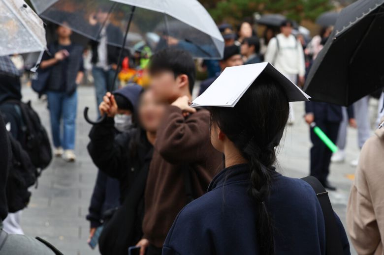 비가 내린 16일 오후 2025학년도 대입 수시모집 논술시험이 열린 서울 종로구 성균관대학교에서 시험을 마친 한 수험생이 종이로 비를 피하고 있다. 연합뉴스