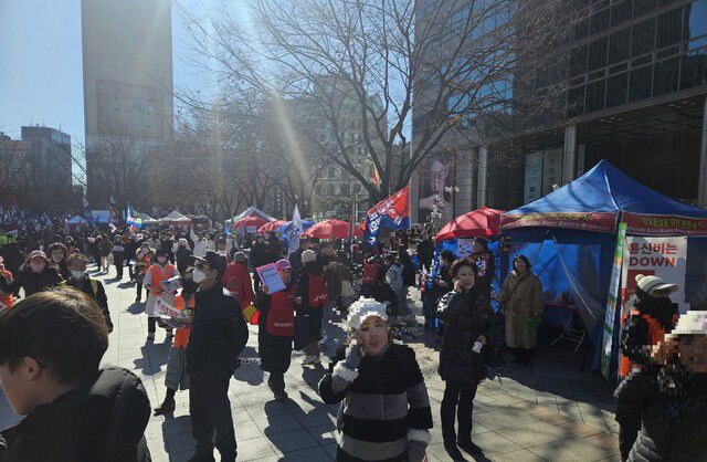 2025년 1월25일 서울 광화문역 6번 출구 동화면세점 앞 모습. 집회 현장 한쪽으로 ‘자유통일을 위한 천만조직’ 천막과 퍼스트모바일 사업 홍보 배너가 보인다. 주황 조끼를 입은 이들은 헌금을 걷는 역할을, 빨간 조끼를 입은 이들은 자유통일당 가입 신청을 받는다. 류석우 기자