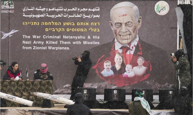 2월20일(현지시각) 가자지구 남부 칸 유니스에 있는 적십자사에 인질의 주검 4구가 담긴 관을 인도하기 전 베냐민 네타냐후 이스라엘 총리 얼굴이 악마처럼 그려진 그림 앞에서 인도식을 하고 있다. 칸유니스/AP 연합뉴스