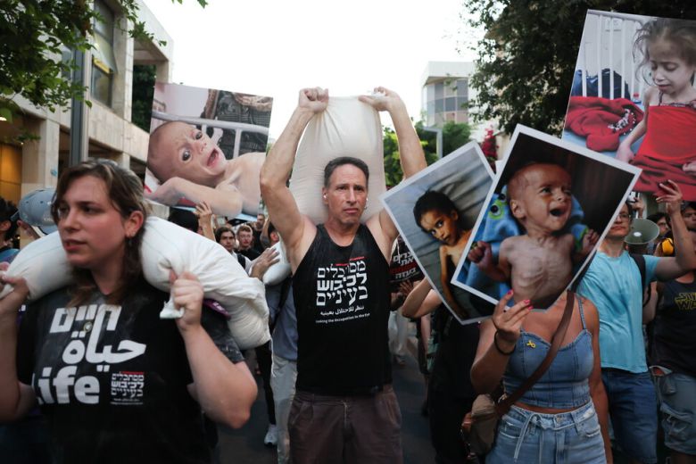 이스라엘과 아랍 활동가들이 밀가루 포대를 지고 굶주린 가자 어린이들의 사진을 들고 가자 전쟁과 그로 인한 기아를 모두 끝내자고 요구하며 22일 이스라엘 텔아비브 시내를 행진하고 있다. EPA 연합뉴스