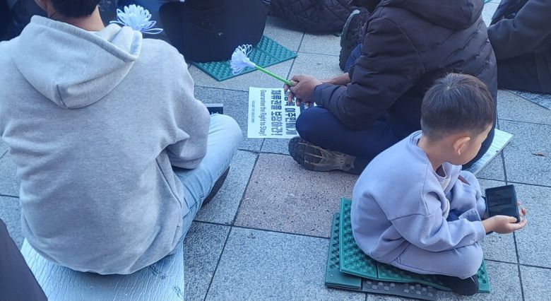 지난 16일 대구시 달서구 성서공단역 앞에서 열린 고 뚜안씨의 거리 추모제에서 부모와 함께 온 아이가 휴대폰을 보고 있다. 이문영 기자