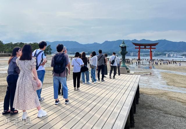 관광객이 이쓰쿠시마 신사에서 도리이를 배경으로 기념사진을 찍기 위해 길게 줄을 서 있다.