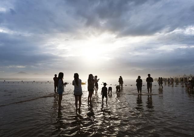 지난 26일 다대포해수욕장을 찾은 여행객들이 짙은 구름 속에서 잠시 햇살이 비치자 인증사진을 찍고 있다. 근래 노을 명소로 각광받는 해변이다.