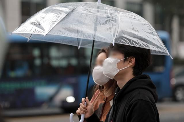 비가 내린 21일 서울 종로구 세종대로 인근에서 우산과 마스크를 쓴 시민들이 신호를 기다리고 있다. 뉴시스
