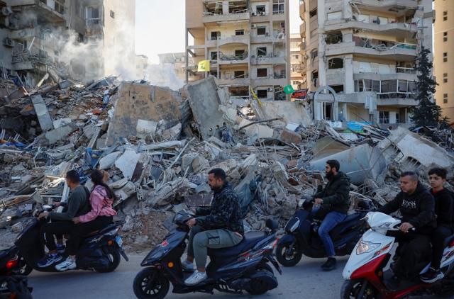 레바논 수도 베이루트 남부에 위치한 타유네 지역에서 지난해 11월 이스라엘군 폭격에 맞아 무너진 건물 앞으로 주민들이 스쿠터를 타고 지나가고 있다. 베이루트=로이터 연합뉴스