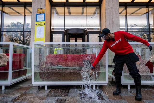 영국 런던의 석유 대기업 쉘 본사 앞에서 12일 국제환경단체 그린피스 소속 환경운동가가 소품이 물에 잠긴 유리 진열장을 깨며 석유 및 가스 산업이 전 세계 사람들의 삶과 생태계를 파괴하는 극심한 기상 현상을 심화시키고 있다는 퍼포먼스를 보이고 있다. 런던=로이터 연합뉴스