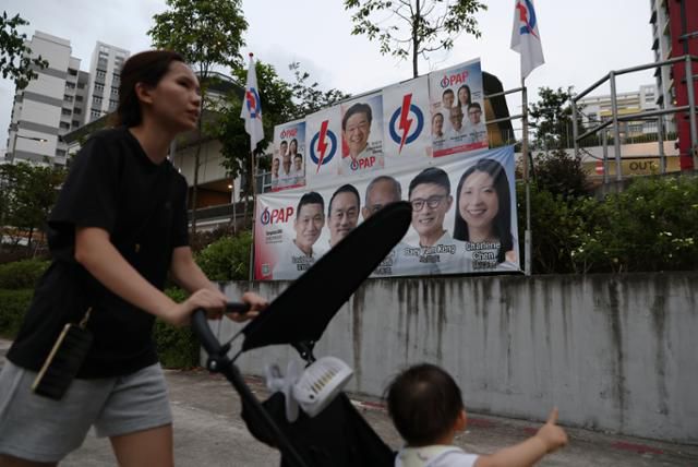 지난달 30일 싱가포르 주택가에서 한 시민이 인민행동당(PAP) 총선 후보자들의 얼굴이 담긴 현수막 앞을 지나고 있다. 싱가포르=EPA 연합뉴스