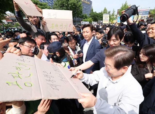 민심을 청취하는 '경청 투어'에 나선 이재명 더불어민주당 대선 후보가 7일 전북 전주시 완산구 풍남문 인근에서 공판 연기를 환영하는 지지자의 응원 피켓에 사인을 해주고 있다. '공판 연기 환영, 대통령은 국민이 뽑습니다'라고 적힌 피켓에 이 후보는 '맞습니다'라고 쓰고 있다. 전주=뉴시스
