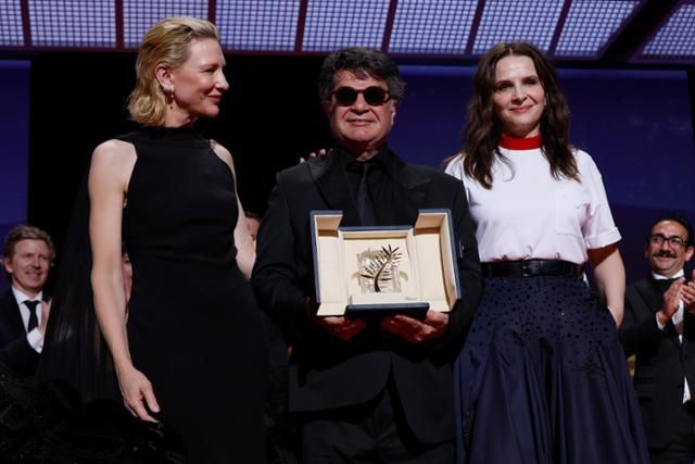 자파르 파나히 감독이 24일 제78회 칸국제영화제에서 황금종려상을 수상한 후 경쟁 부문 심사위원인 호주 배우 케이트 블란쳇(왼쪽)과 심사위원장인 프랑스 배우 줄리엣 비노시와 함께 사진 촬영에 응하고 있다. 칸=AP 연합뉴스