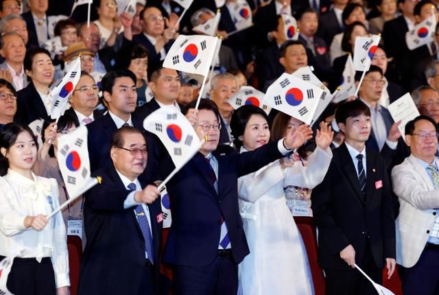 이재명 대통령과 김혜경 여사가 지난 15일 서울 종로구 세종문화회관에서 열린 제80주년 광복절 경축식에서 참석자들과 태극기를 흔들고 있다. 뉴시스