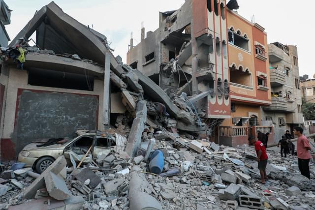 팔레스타인 주민들이 25일 가자지구 중앙 누세이라트 난민캠프에서 이스라엘의 공중 및 지상 공세로 피해를 입은 건물 잔해 주위를 살펴보고 있다. 가자=AFP 연합뉴스