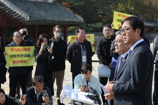 최휘영(오른쪽) 문화체육관광부 장관과 허민 국가유산청장이 7일 서울 종묘에서 종묘 앞 개발 규제 완화 관련 대법원 판결에 대한 입장 발표 기자회견을 진행하는 가운데 세운4구역 주민 대표들이 개발 지연에 항의하는 피켓을 들고 있다. 연합뉴스