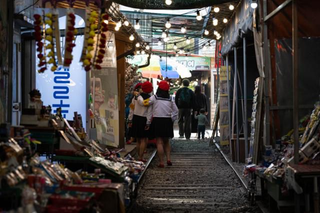 철길 양옆으로 상인들의 물건이 잔뜩 쌓여 있는 가운데 관광객이 교복을 입고 기념촬영을 하고 있다.