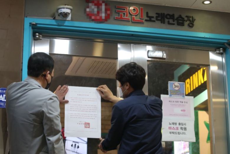 지난해 가을 경기도의 한 코인노래연습장 입구에 공무원들이 집합금지 명령서를 붙이고 있다. [연합]