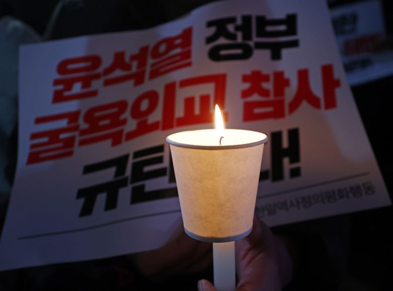 13일 오후 서울 중구 서울파이낸스빌딩 앞에서 열린 윤석열 정부의 강제동원 해법 발표 규탄 집회에서 참가자가 촛불과 피켓을 들고 있다. [연합]