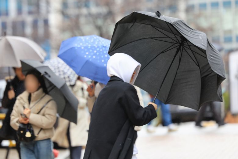 지난 21일 오후 서울 중구 명동에서 한 시민이 바람에 날리는 우산을 잡고 있다. [연합]