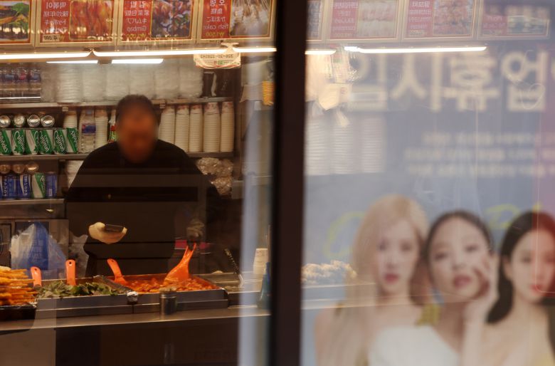 최근 서울 중구의 한 임시휴업한 가게 출입문에 장사 준비를 하는 자영업자 모습이 비치고 있다.  [뉴시스]