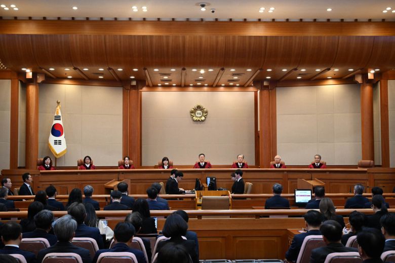 윤석열 전 대통령의 파면 선고가 이루어진 헌법재판소 대심판정의 정면 벽에 설치된 헌재의  상징 휘장. 국화인 무궁화 속에 헌법이라는 글자로부터 ‘공정한 빛’이 확산되는 모습을 표현하고 있다. 가운데 원의 흰색은 ‘평등’을 , 무궁화 꽃잎의 자색은 국민의 신뢰를 바탕으로 한 헌재의 ‘권위’를 나타낸다. [연합]